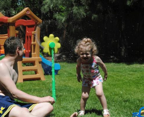 Father and daughter playing in sprinkler