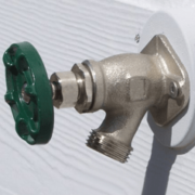 Close-up of an outdoor hose bib spigot mounted on a wall, featuring a metal faucet with a sturdy handle and threaded connection for garden hoses