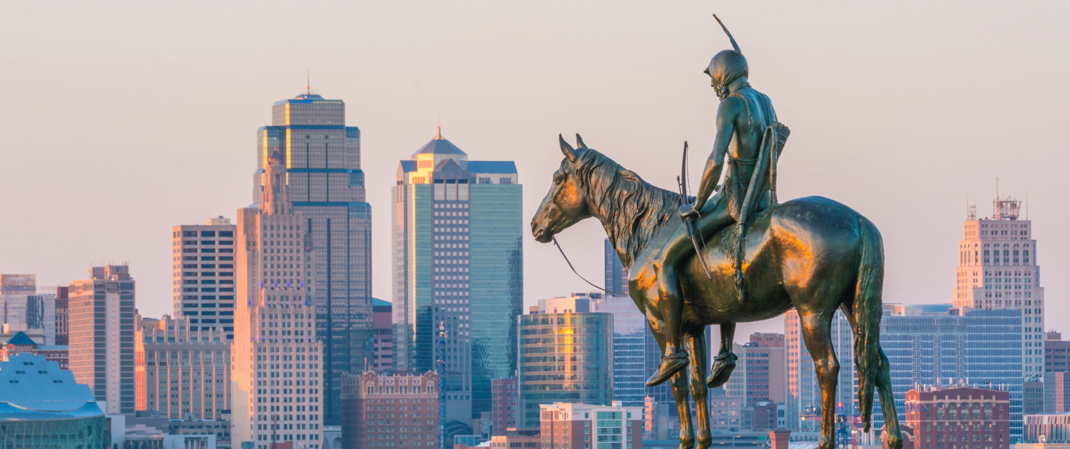 Statue of a cowboy overlooking a city skyline at sunset.