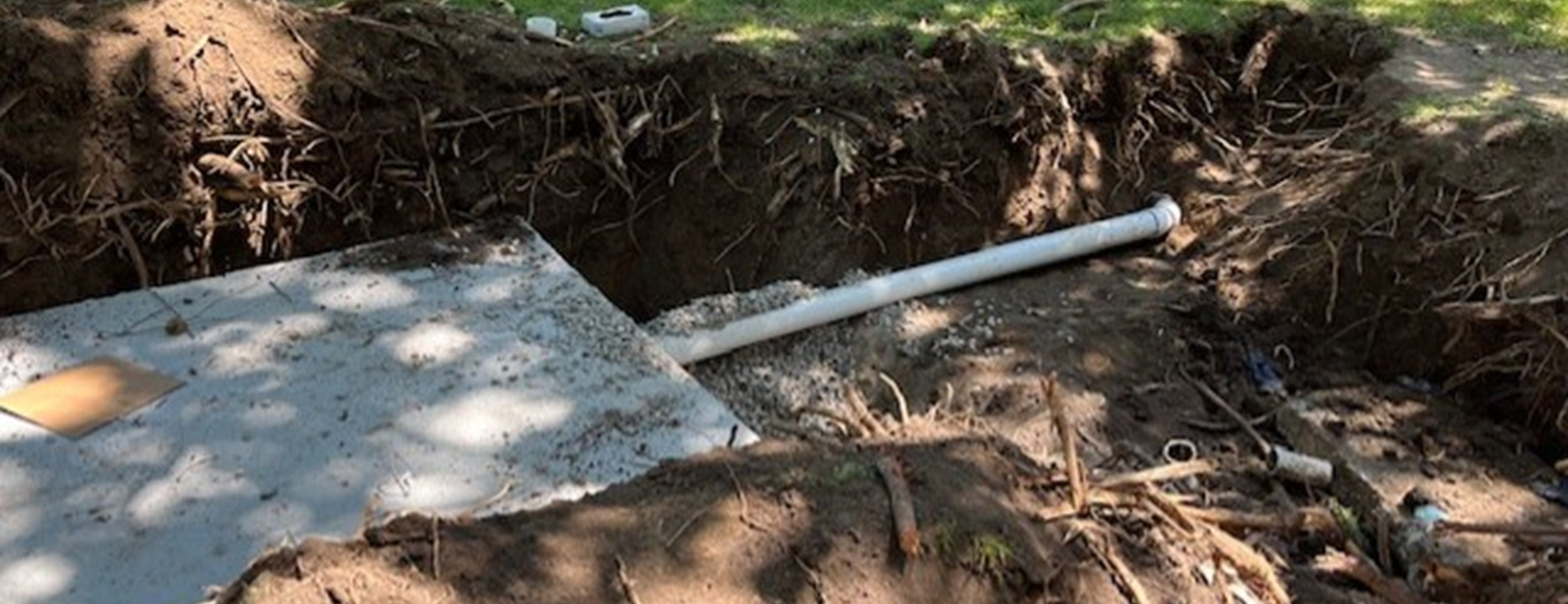 Concrete septic system with a durable holding tank partially buried in the ground, featuring a sturdy lid for access. Surrounding landscape includes gravel and grass, emphasizing the tank's efficient and environmentally friendly design for wastewater management.